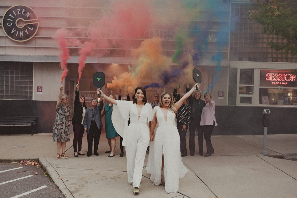 Two brides celebrate their wedding with a rainbow smoke bomb in downtown Asheville, NC