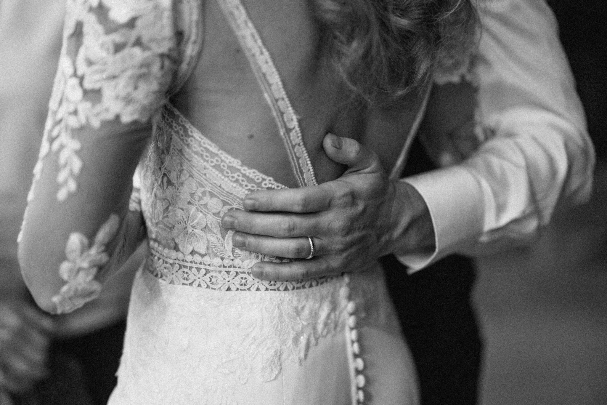 asheville wedding photographer A close-up, black-and-white photo by an Asheville wedding photographer captures a man's hand with a wedding ring gently resting on the back of a woman wearing a lace wedding dress as they share a dance.