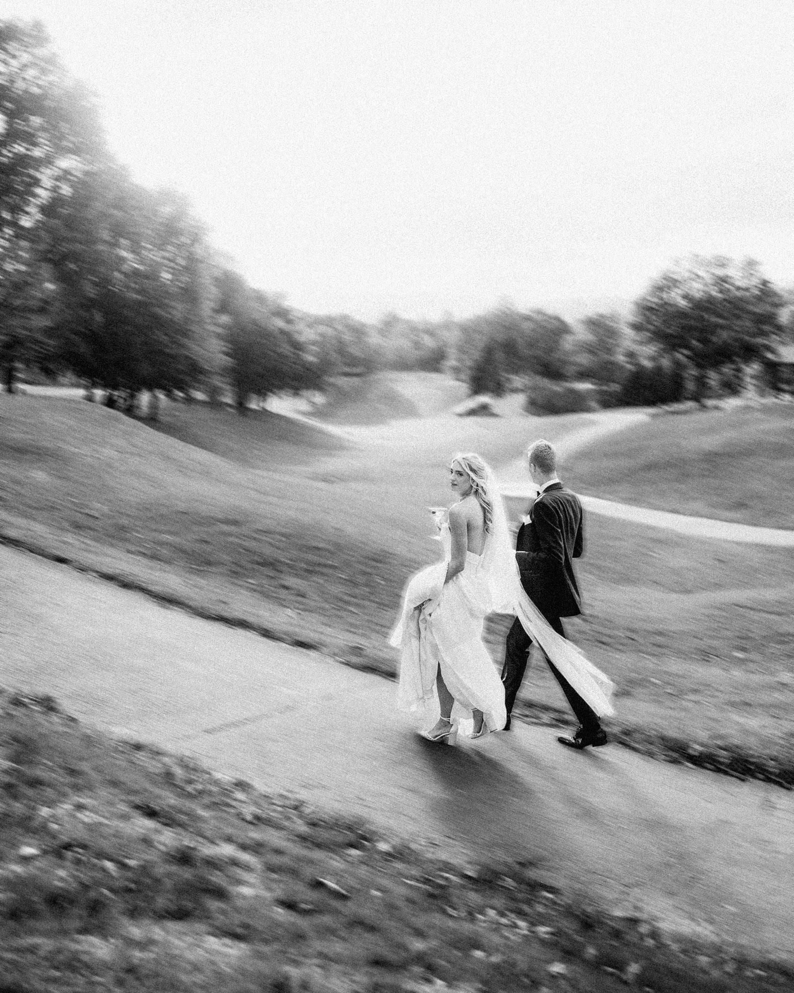 Bride and Groom in black and white walking through The Omni Grove Park Inn with motion blur on a golf course.