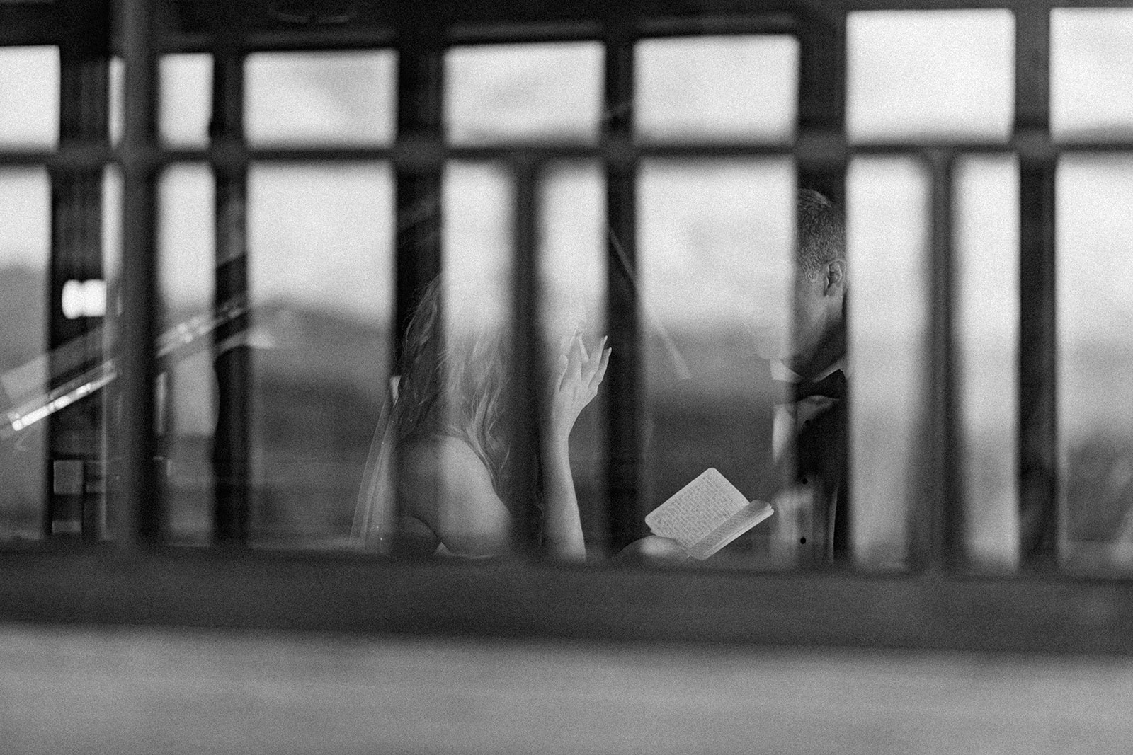 Black and white photo of bride and groom reading private vows through a window at The Grove Park Inn, moments before their Asheville wedding ceremony during Hurricane Helene.
