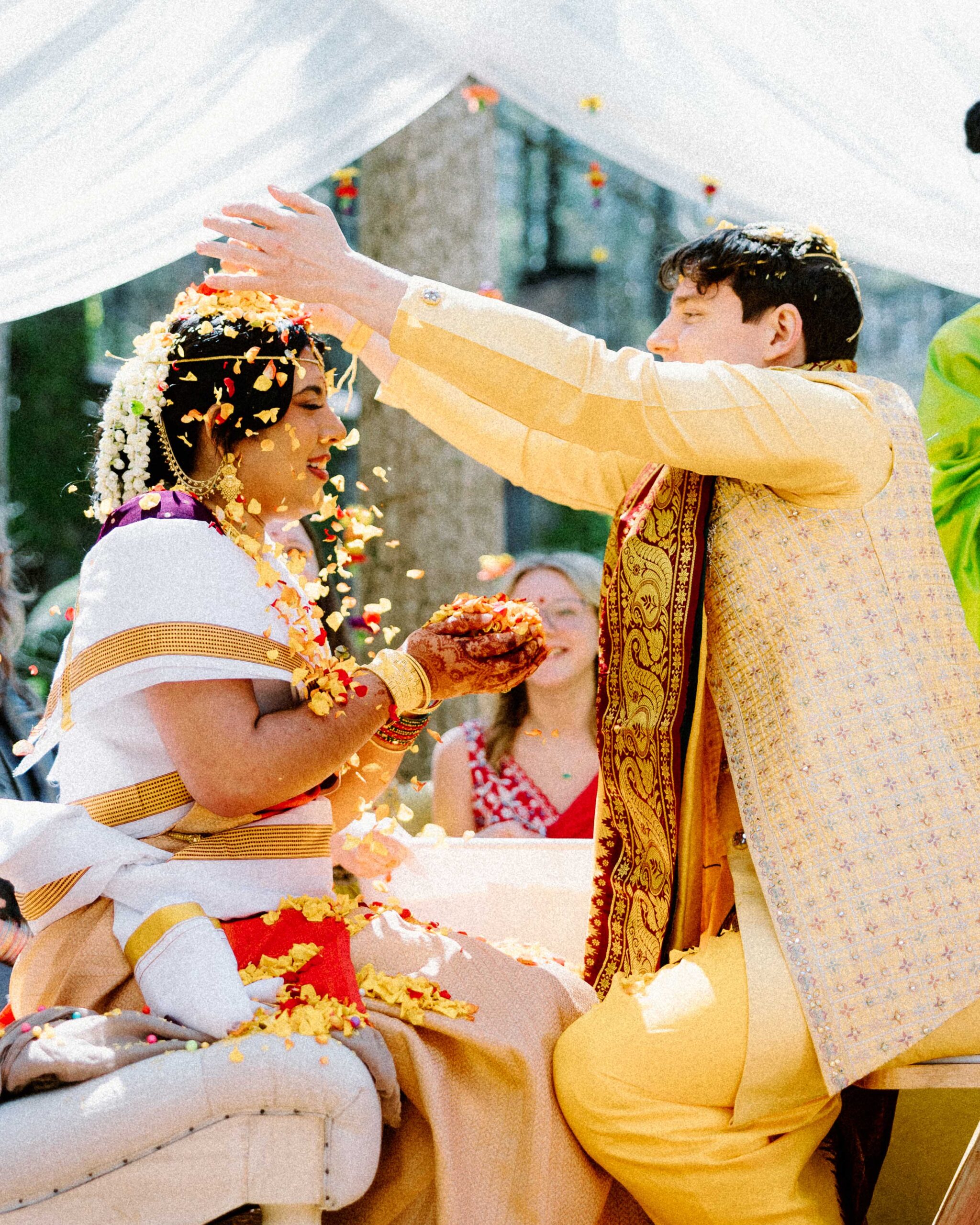 asheville wedding photographer A bride and groom in traditional attire participate in a wedding ceremony; the groom showers the bride with flower petals as they smile joyfully under a decorated canopy, captured beautifully by an Asheville wedding photographer, with guests watching in the background.