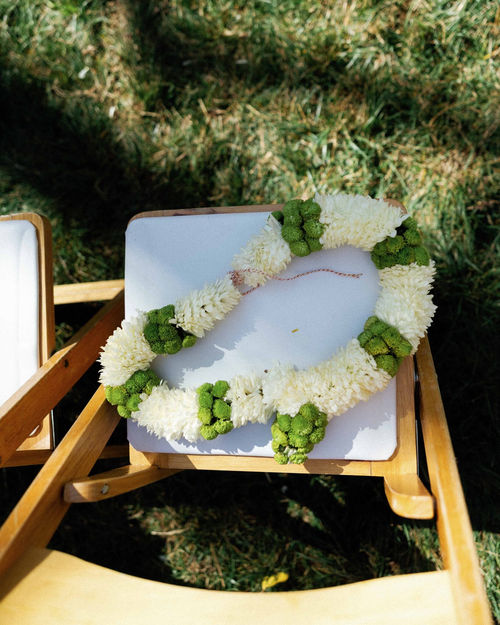asheville wedding photographer A white and green flower garland is draped over the back of a wooden chair set on grass, with sunlight casting shadows on the seat—perfectly captured by an Asheville wedding photographer.
