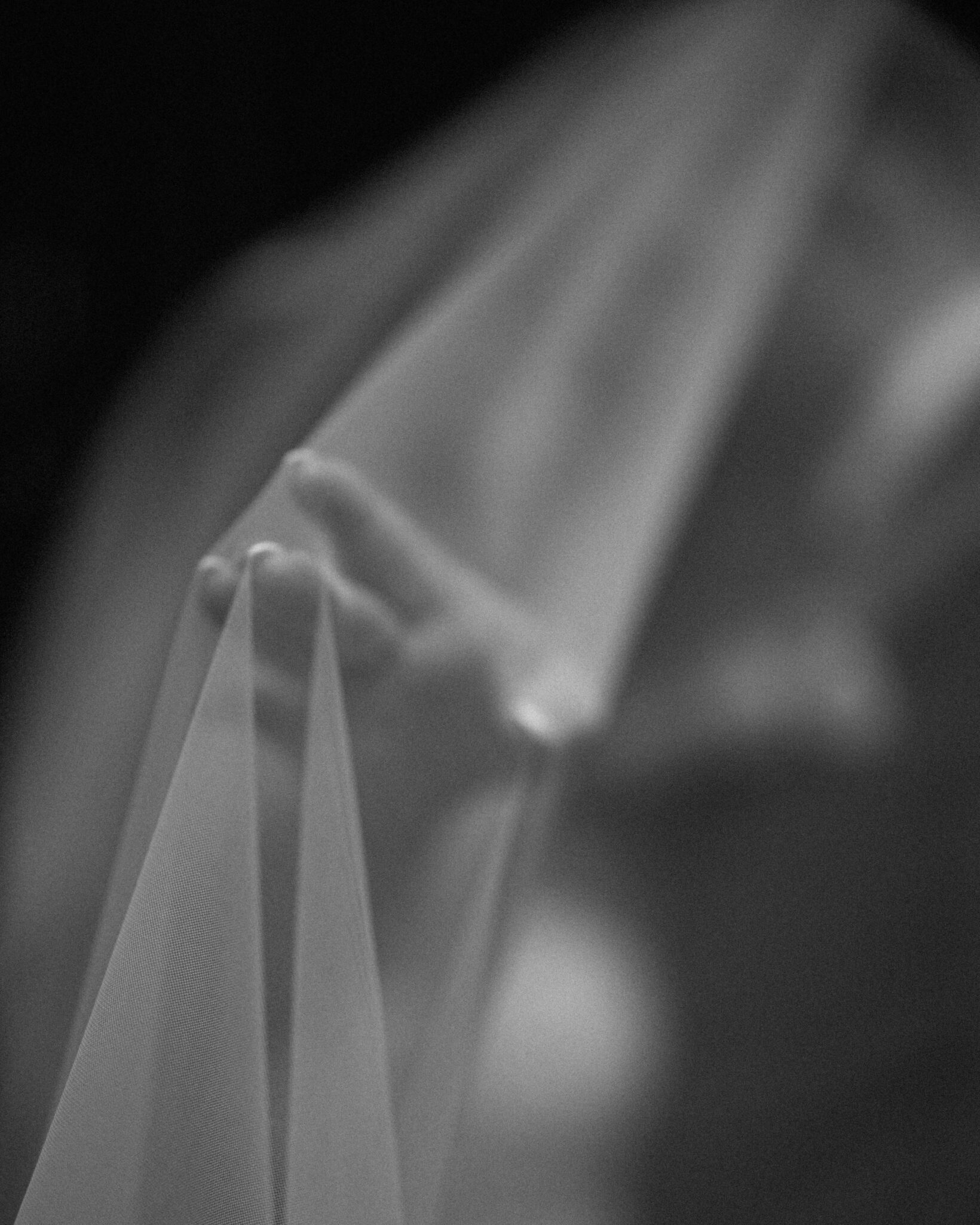 asheville wedding photographer A hand gently lifts a sheer, flowing fabric, possibly a veil, with soft lighting and a blurred background—captured by an Asheville wedding photographer to evoke a dreamy, ethereal effect.