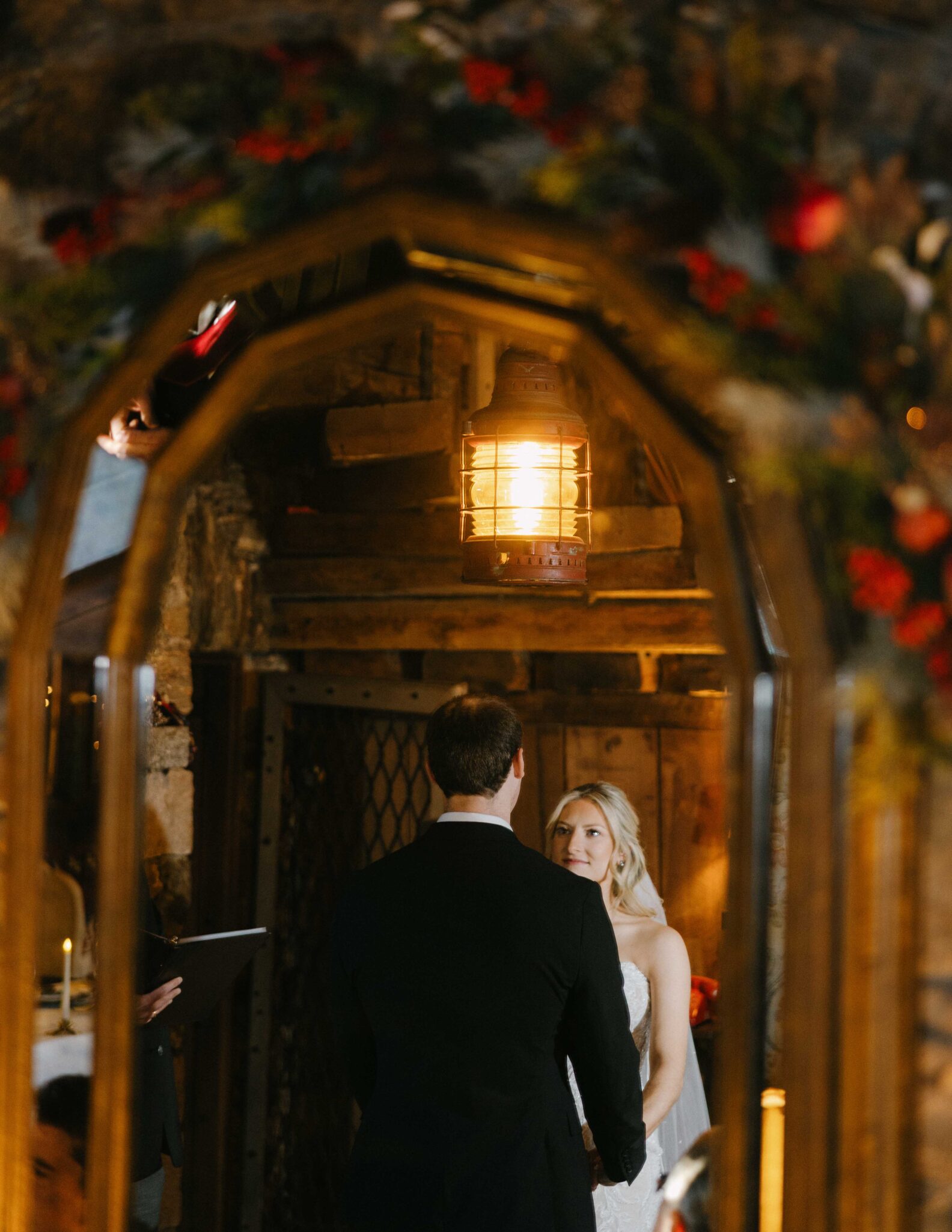 asheville wedding photographer A bride and groom hold hands and face each other during their wedding ceremony, reflected in a rustic mirror with warm lighting and floral decorations—captured beautifully by an Asheville wedding photographer.