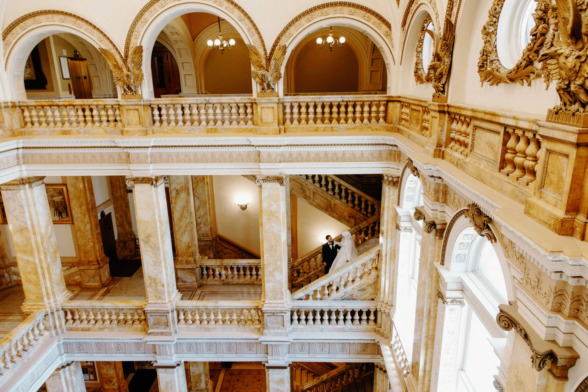 A bride and groom stand together on a grand marble staircase inside an ornate building with high arches—an elegant moment captured by expert Arab wedding photography in Chicago.
