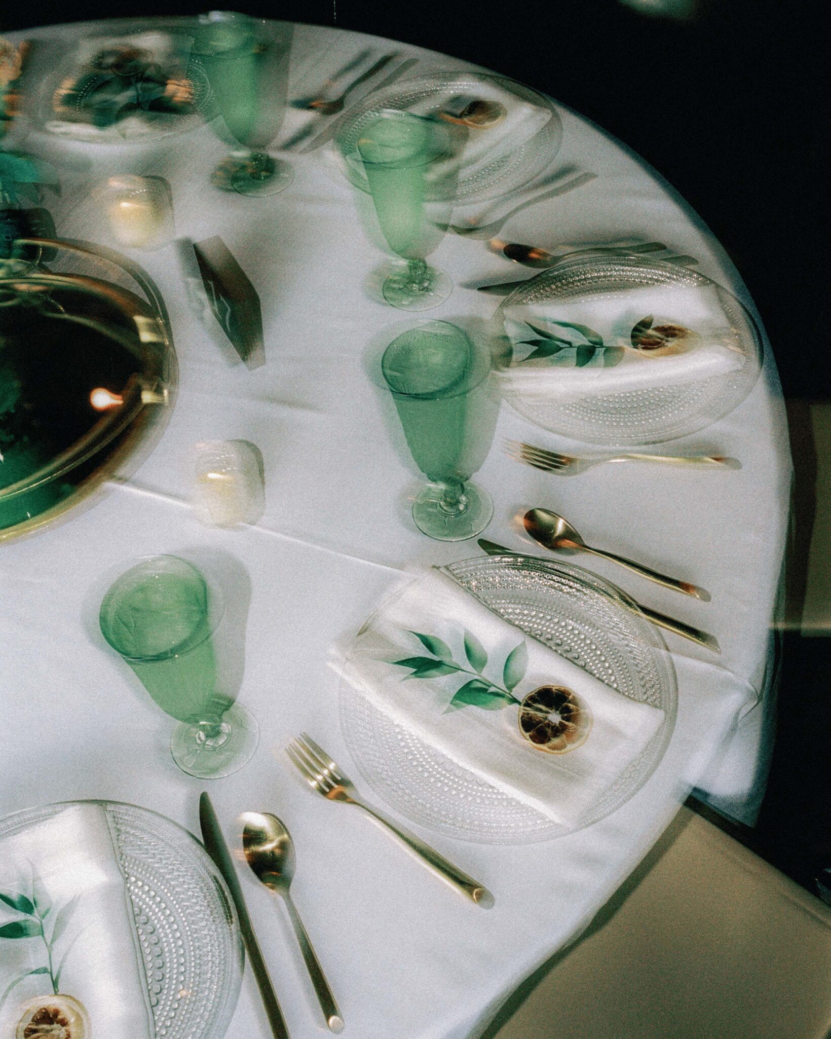 asheville wedding photographer A round table set for a meal with clear plates, silver cutlery, green-tinted glasses, and white napkins decorated with leaves and dried citrus slices, all on a white tablecloth—perfect for film photography at Omni Grove Park weddings.