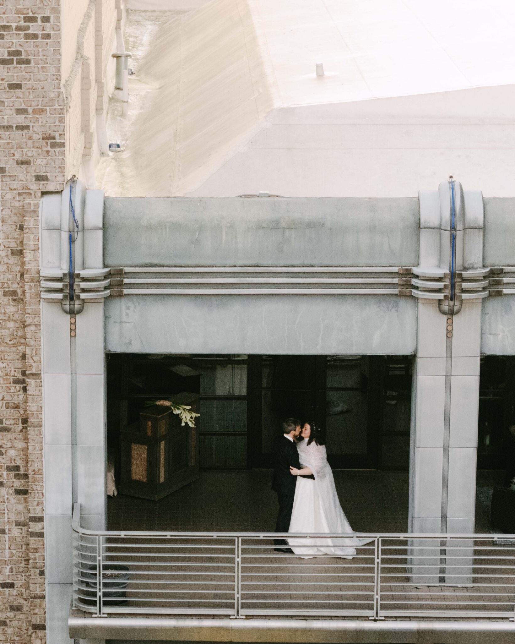 A bride and groom share a romantic embrace on a balcony of a modern, industrial-style building at The Venue Asheville, with city architecture visible in the background—perfect for an unforgettable downtown Asheville wedding.