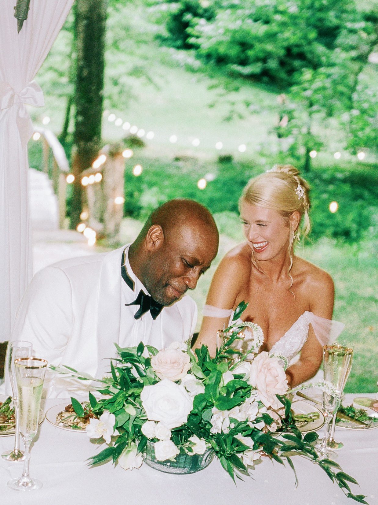 Newlyweds laughing together at their outdoor wedding reception on film