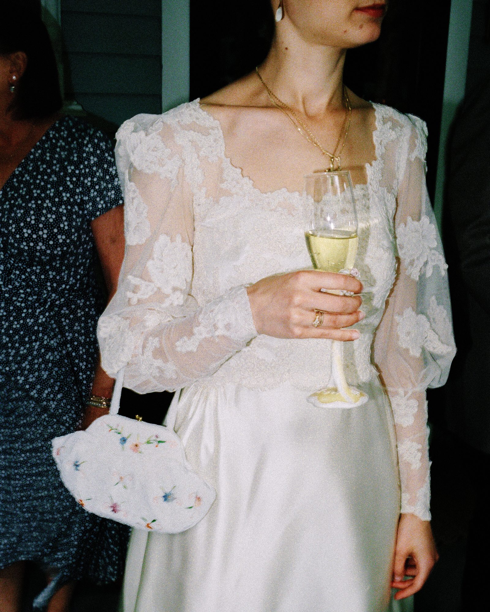 Candid film photograph of a bride holding champagne and a floral clutch