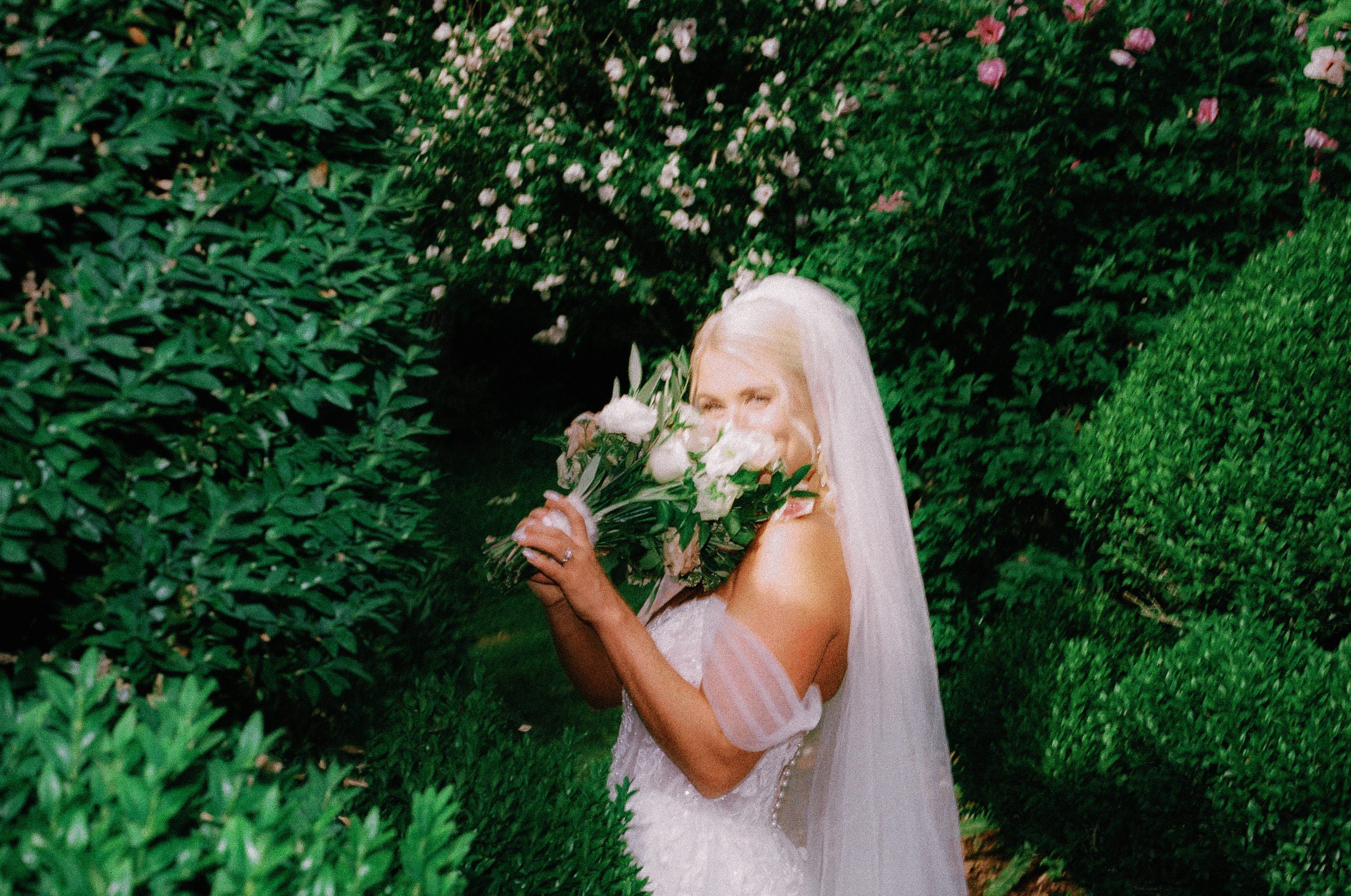 Bride smelling a white flower in a grainy candid 35mm wedding photograph