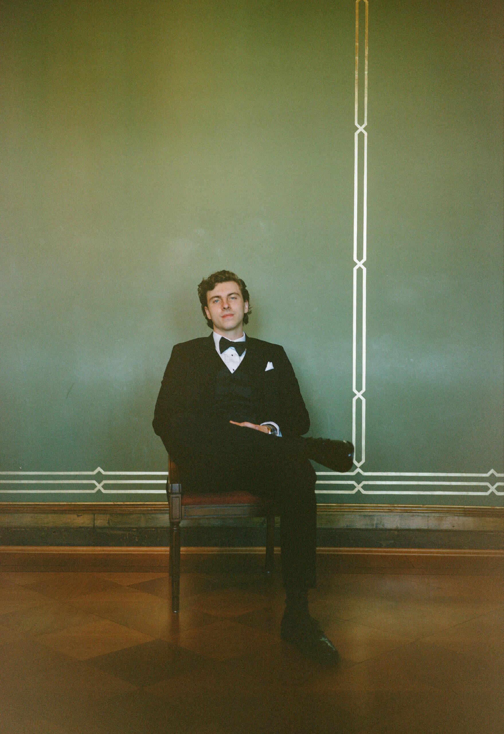 Groom seated alone against a softly lit wall in a medium format style wedding portrait