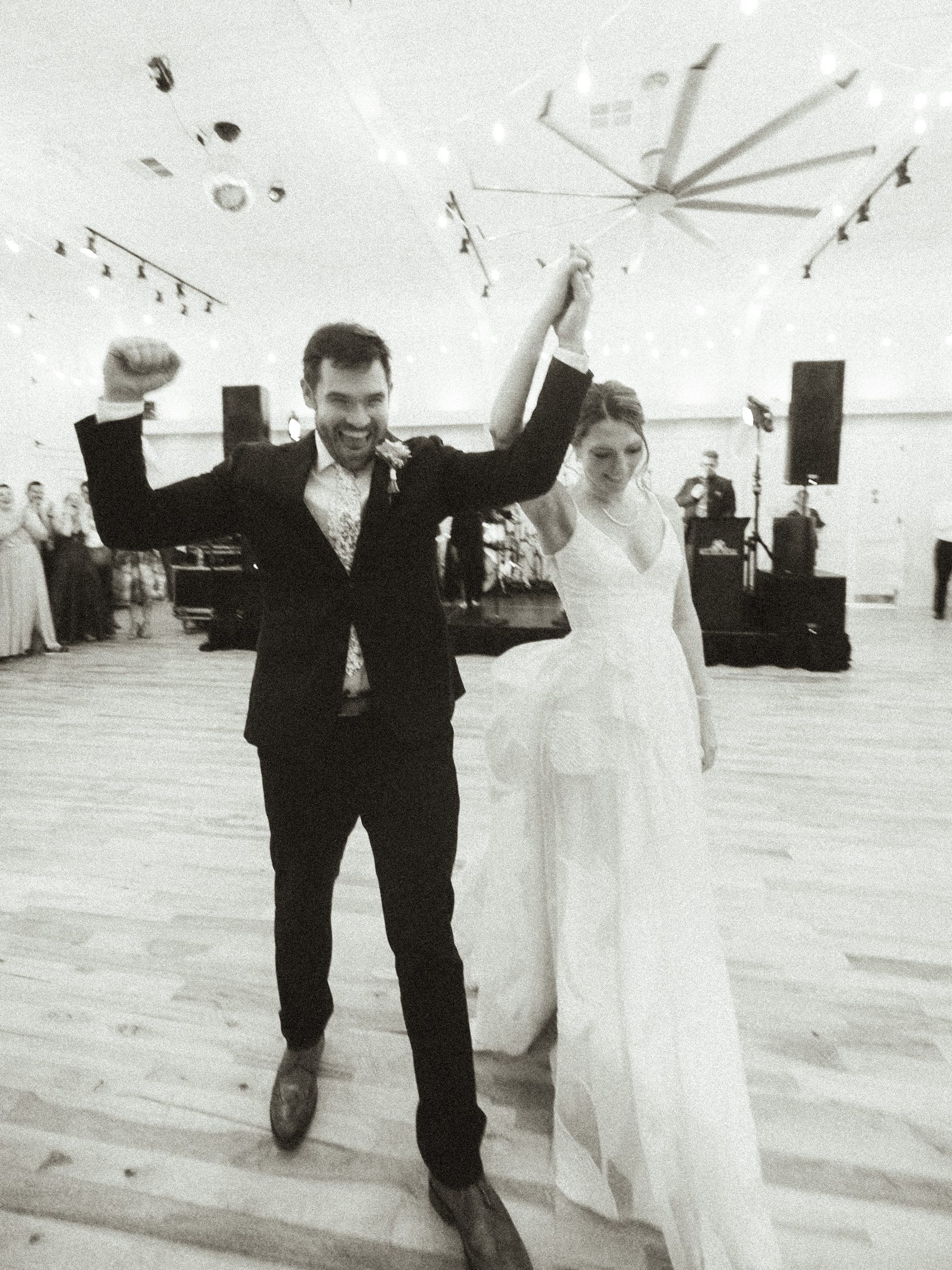 Newlyweds entering the reception with raised arms