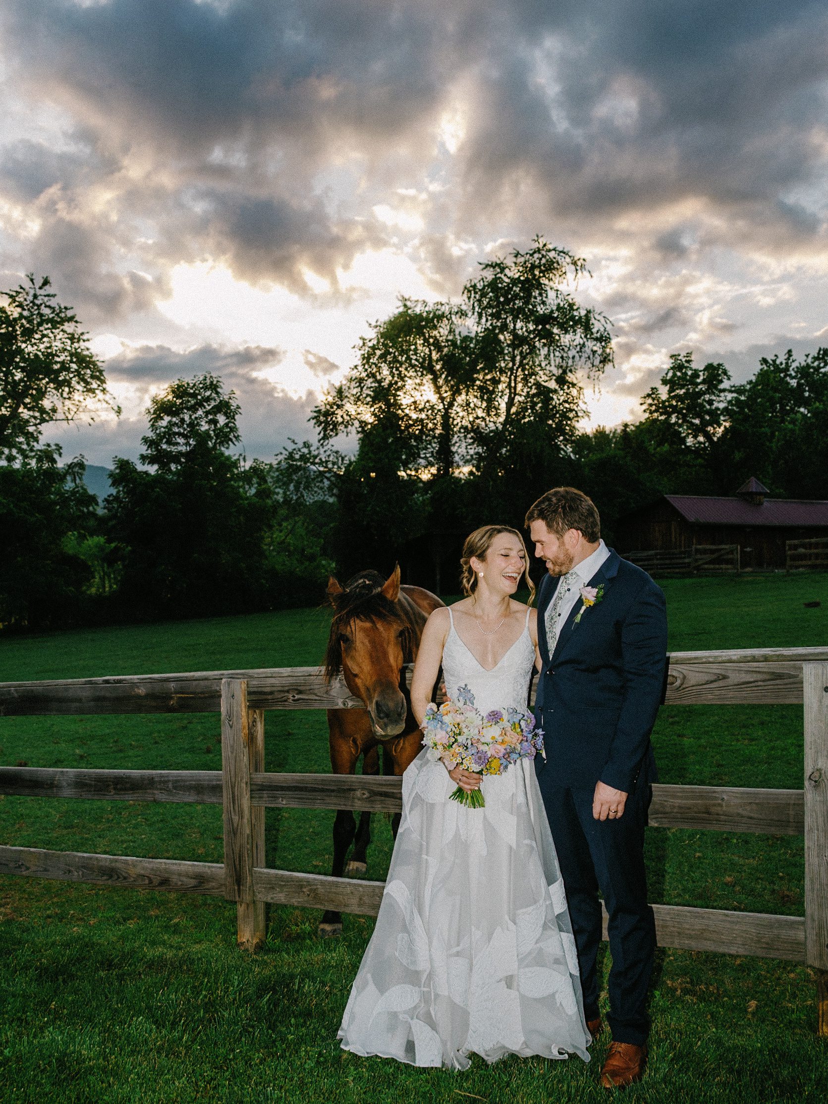 Couple laughing beside a horse at the pasture fence