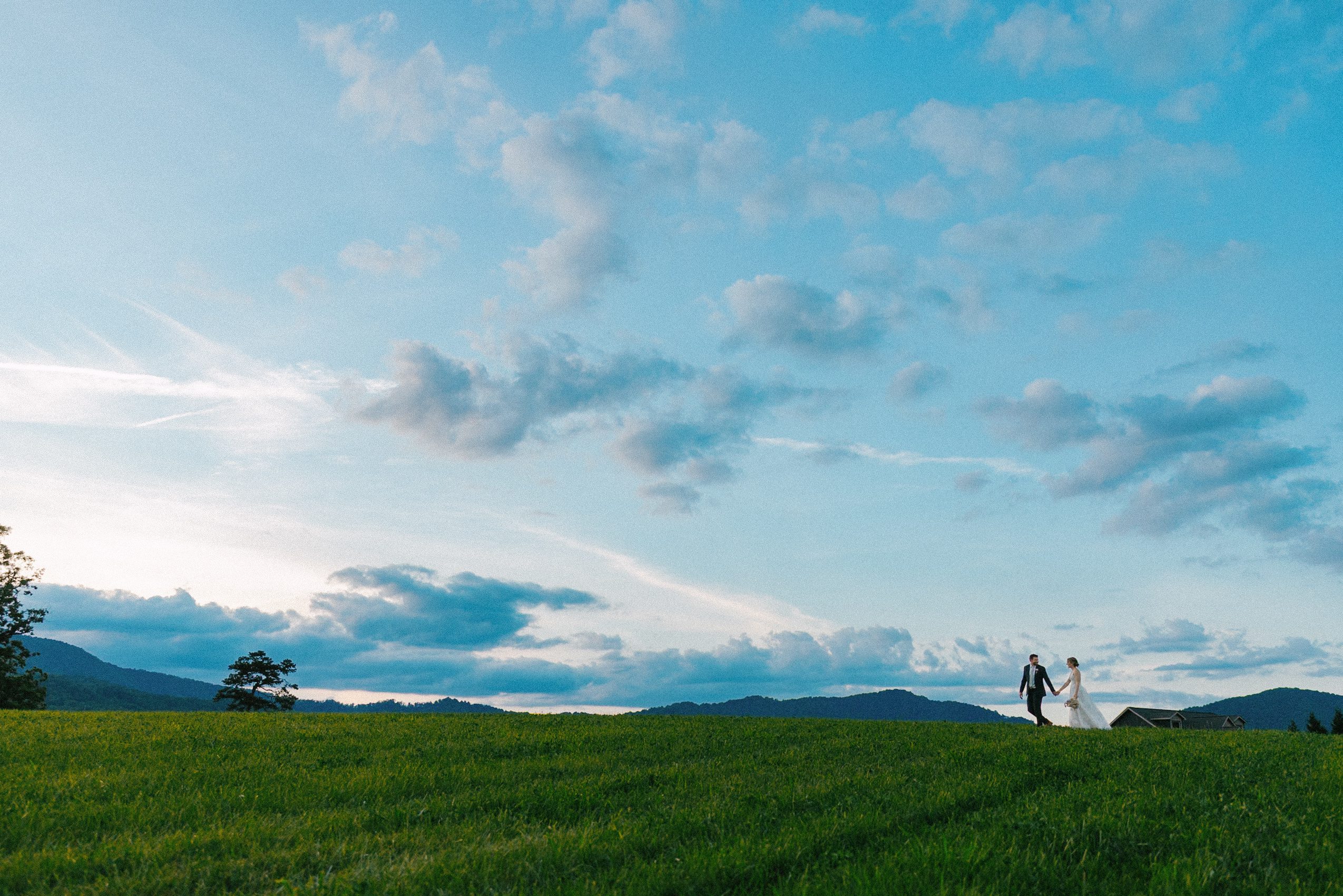 Couple walking through an open field beneath the evening sky