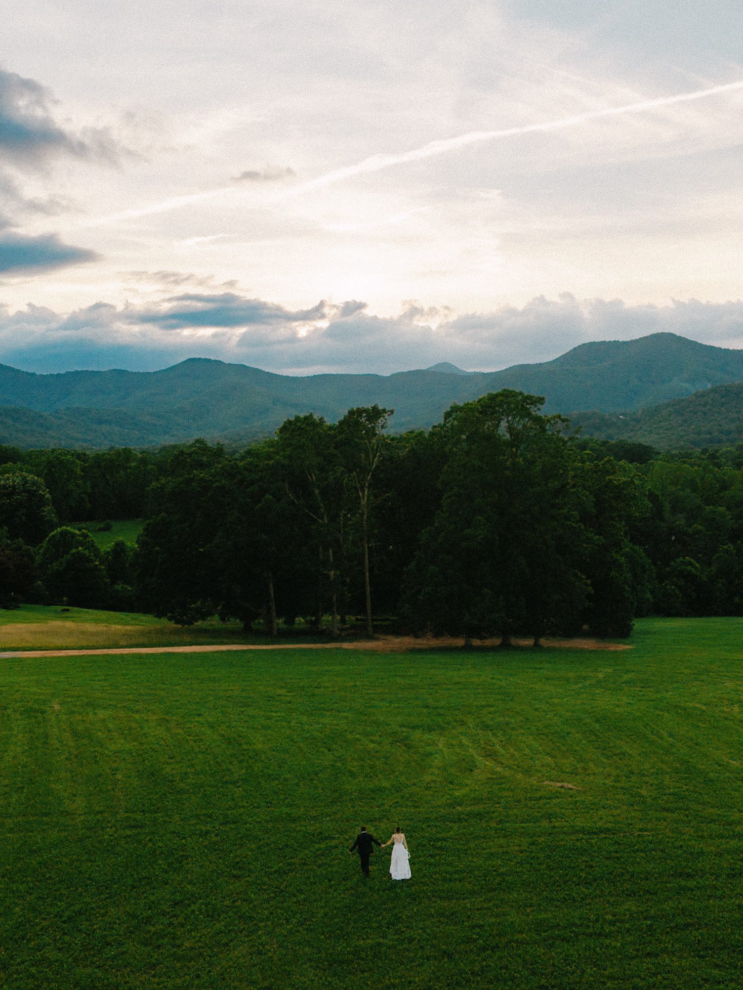 Aerial view of the couple in a field beneath mountain ridges