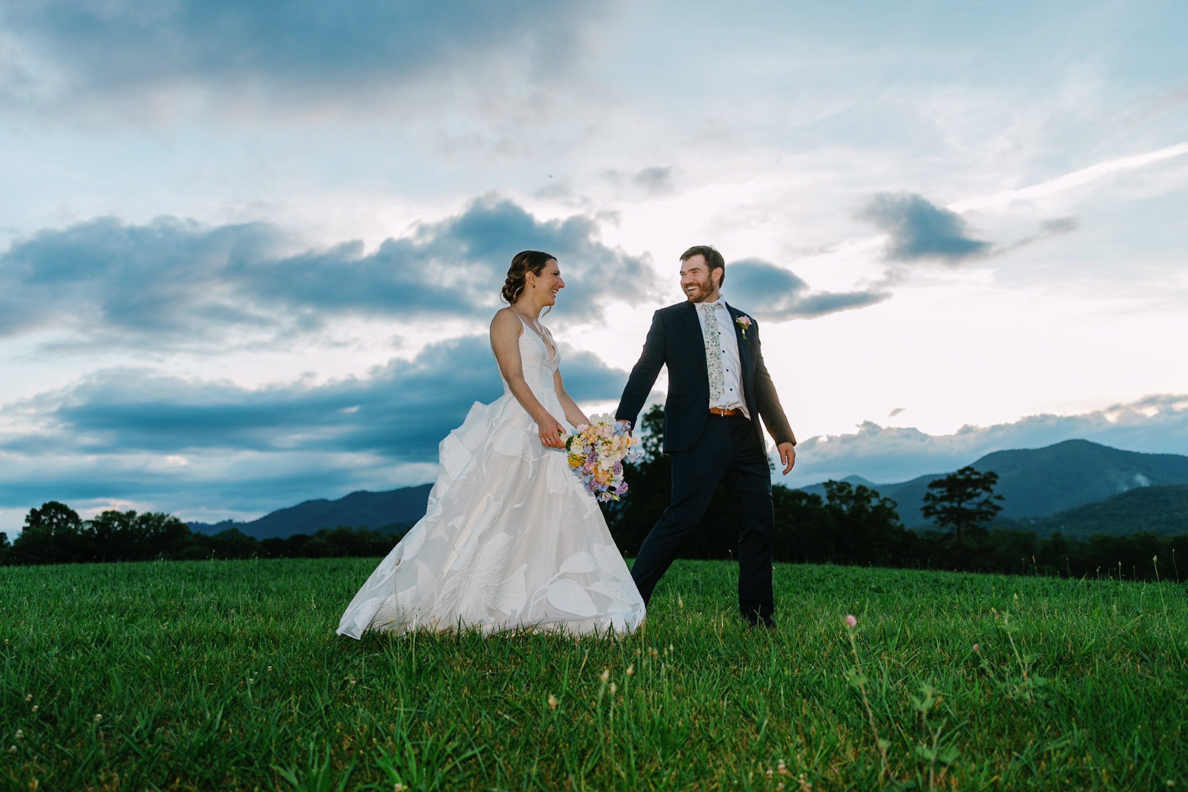 Couple walking hand in hand with mountains and summer clouds behind them