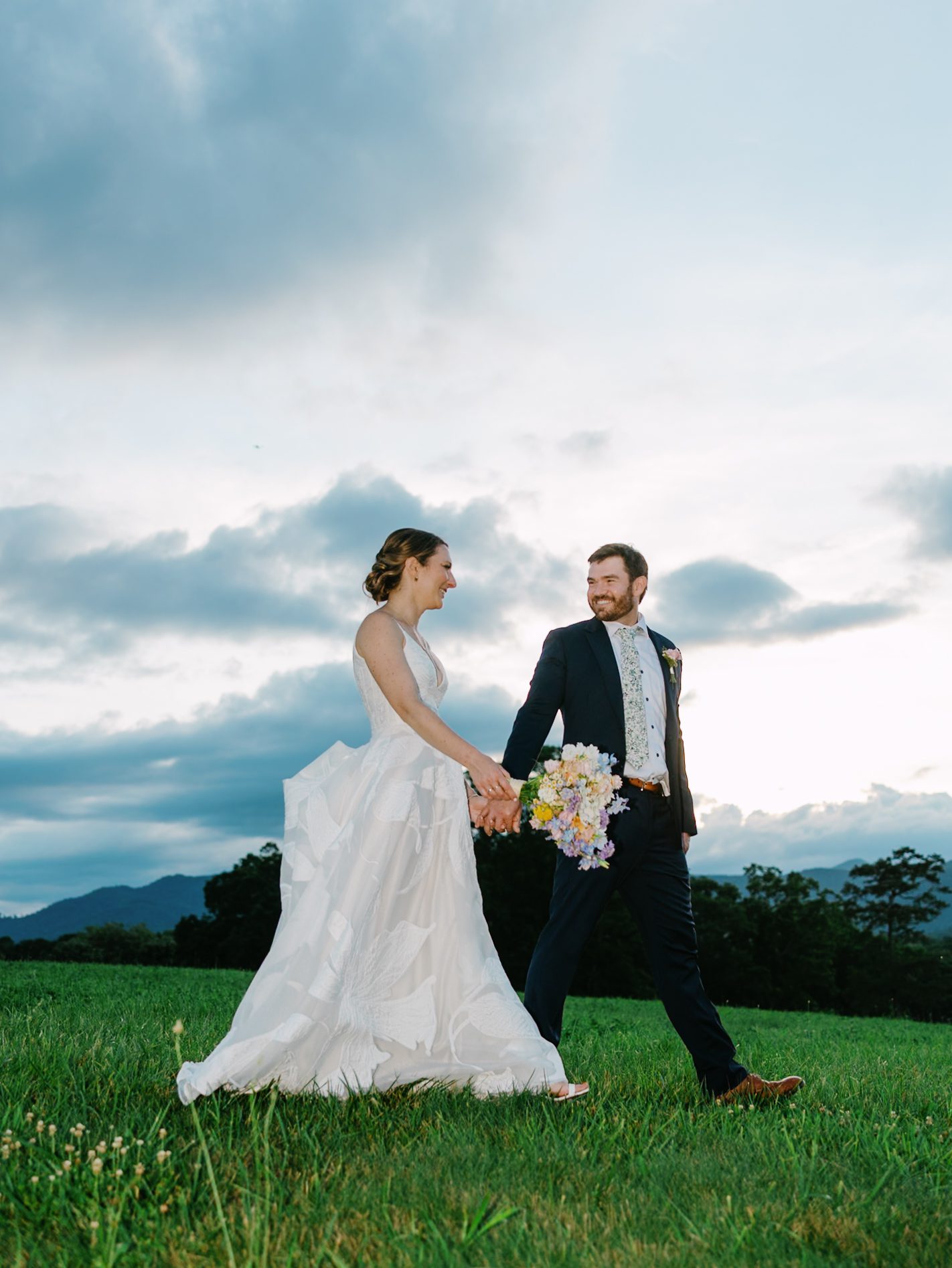Bride and groom laughing while walking through the field
