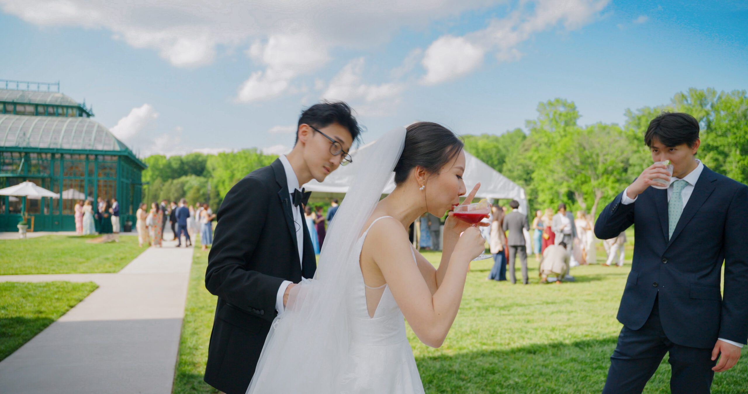 Christie takes a sip from her cocktail beside Hao and a guest, with the Solarium in the background.