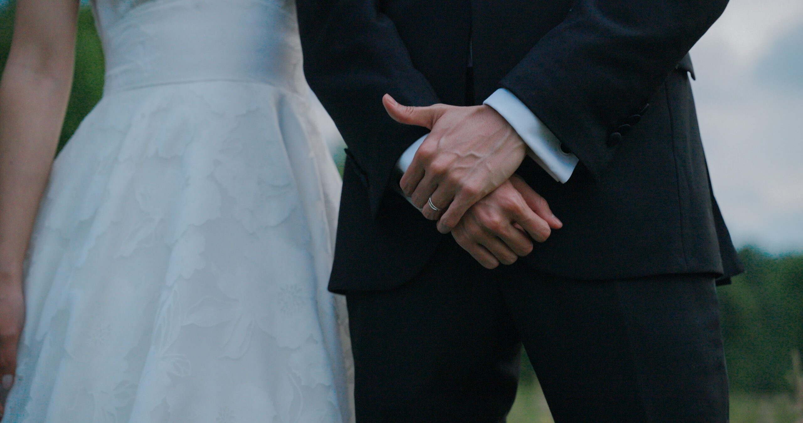 Christie and Hao hold hands, showing the details of her wedding dress and his tuxedo.