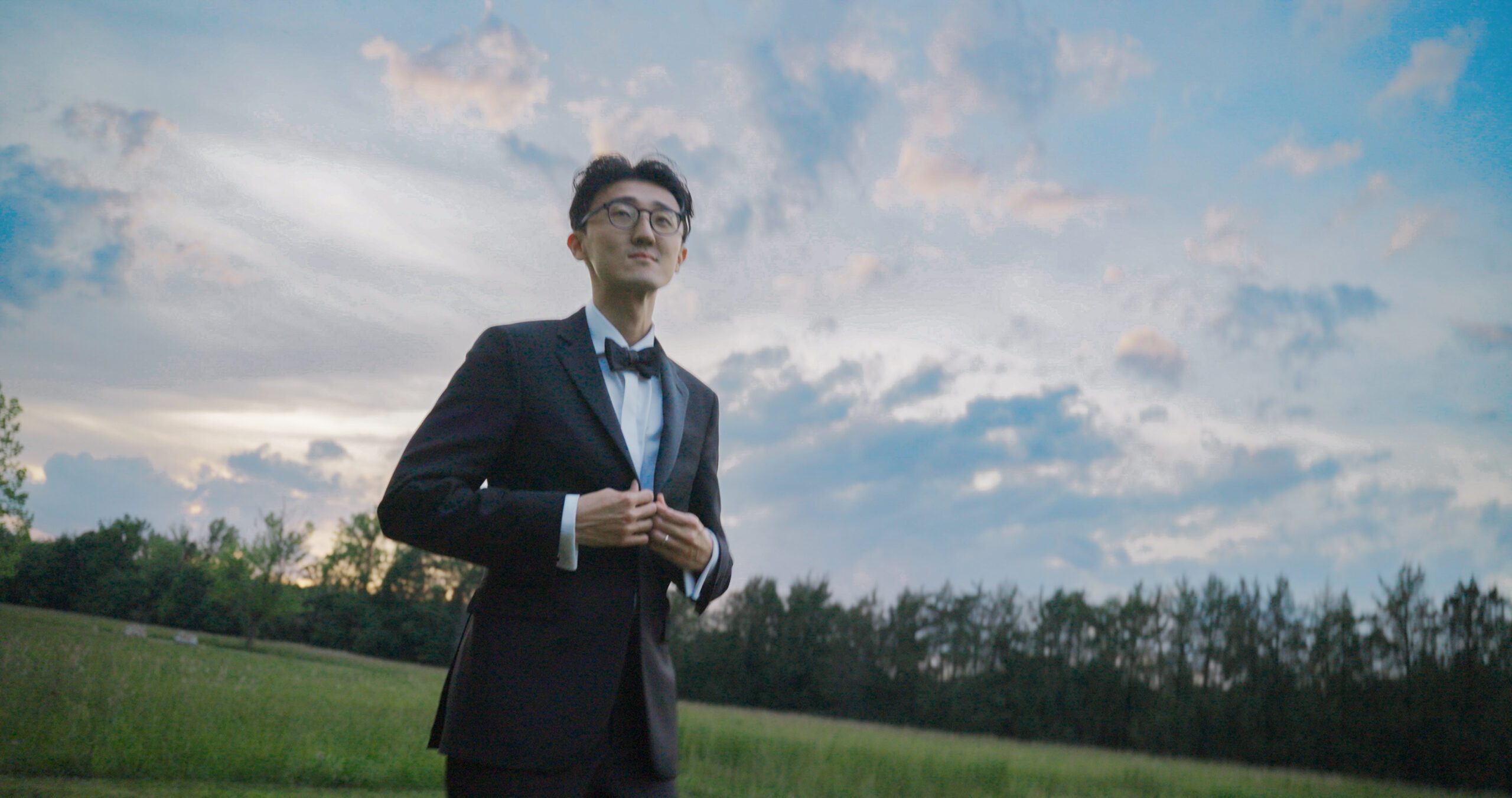 Hao stands in the meadow beneath a cloud-filled sky at Haven Ridge.