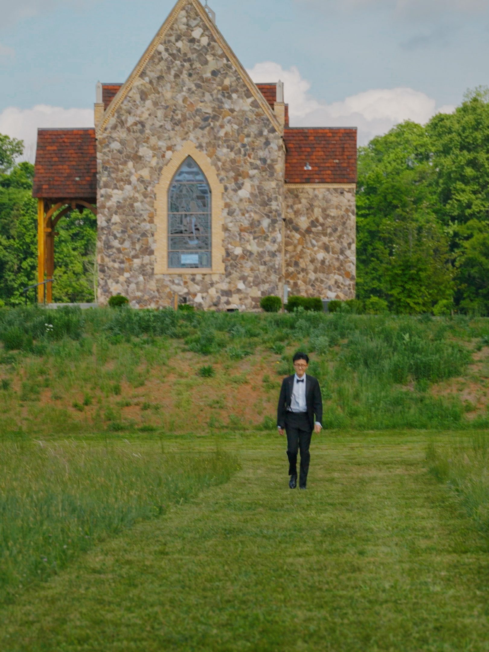 Hao stands in the meadow below the stained-glass window of The Little Chapel at Haven Ridge.