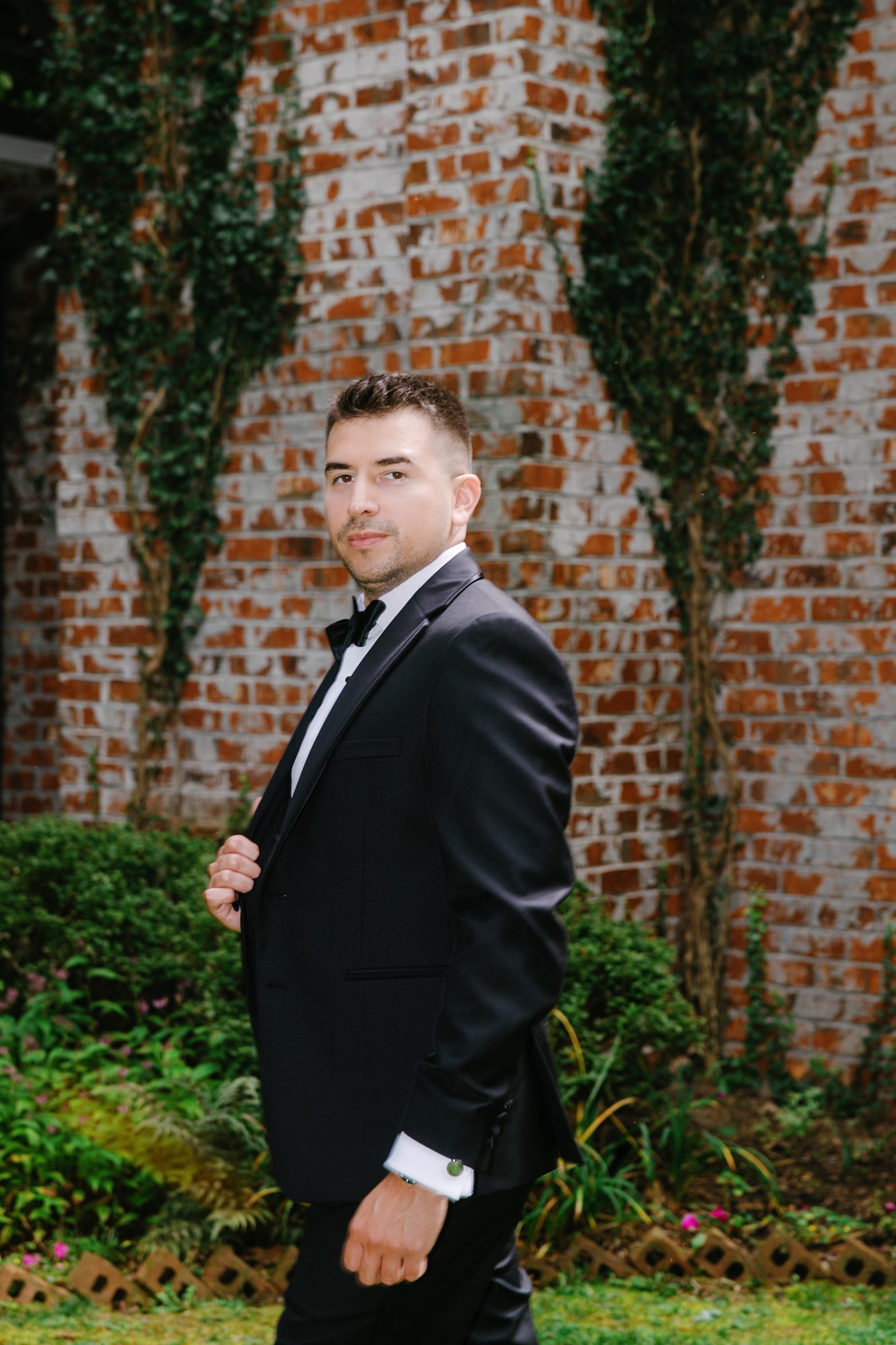Groom in a black tuxedo beside an ivy-covered brick wall, photographed on medium format film at Twickenham House and Hall