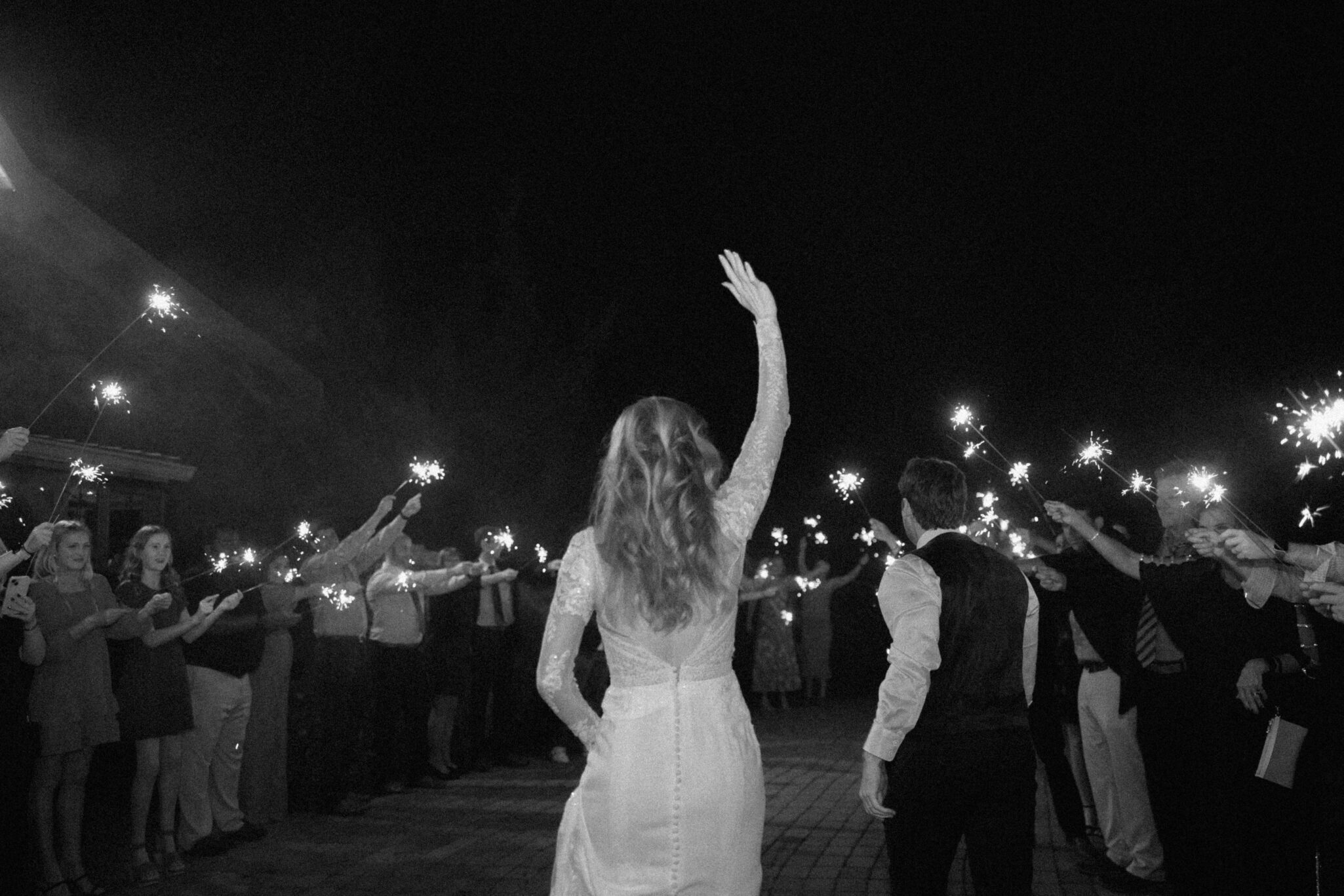 Final image of a bride waving goodbye to friends and family at her wedding. 