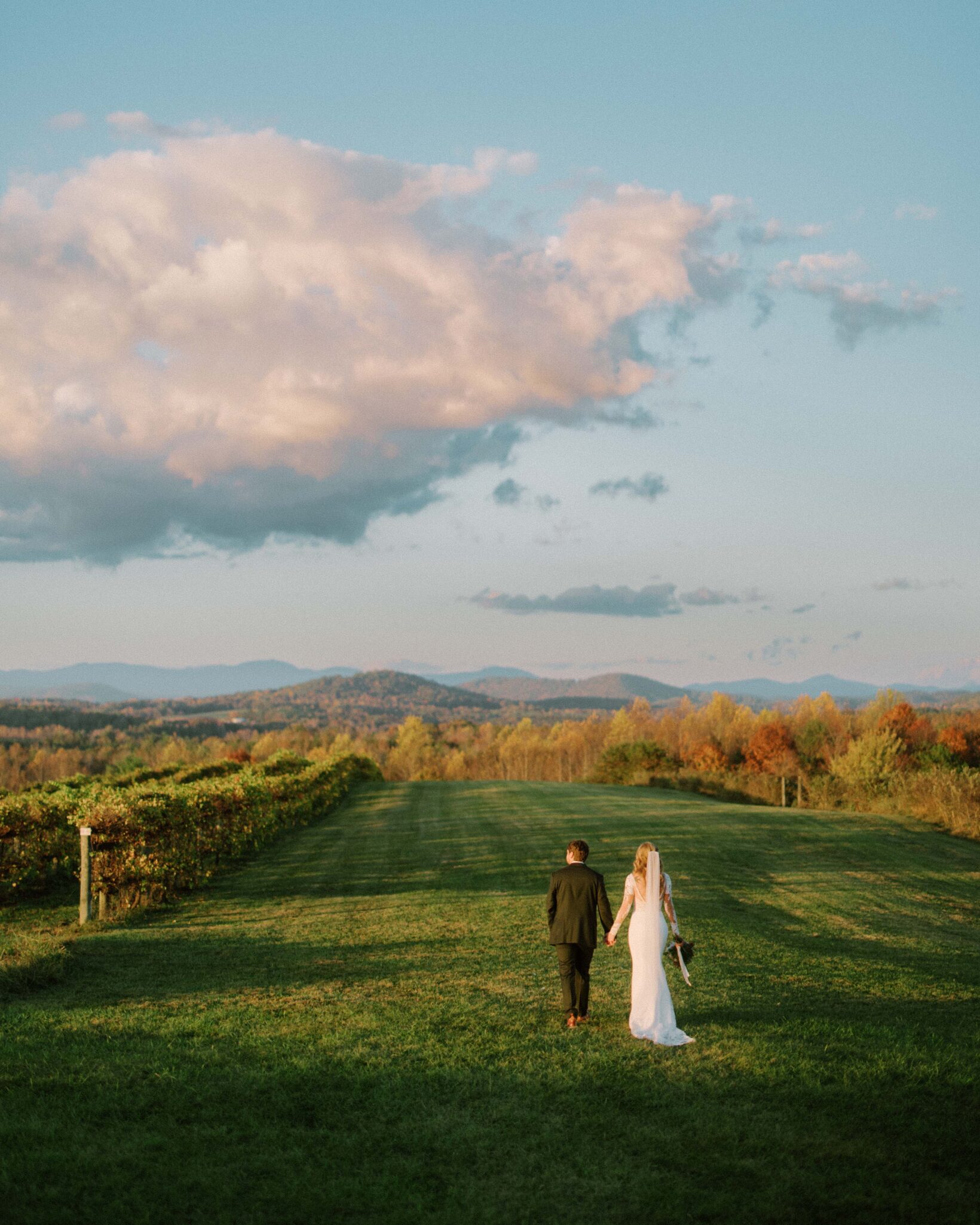 Bride and Groom walk at sunset across a field at Chattooga Belle Farm