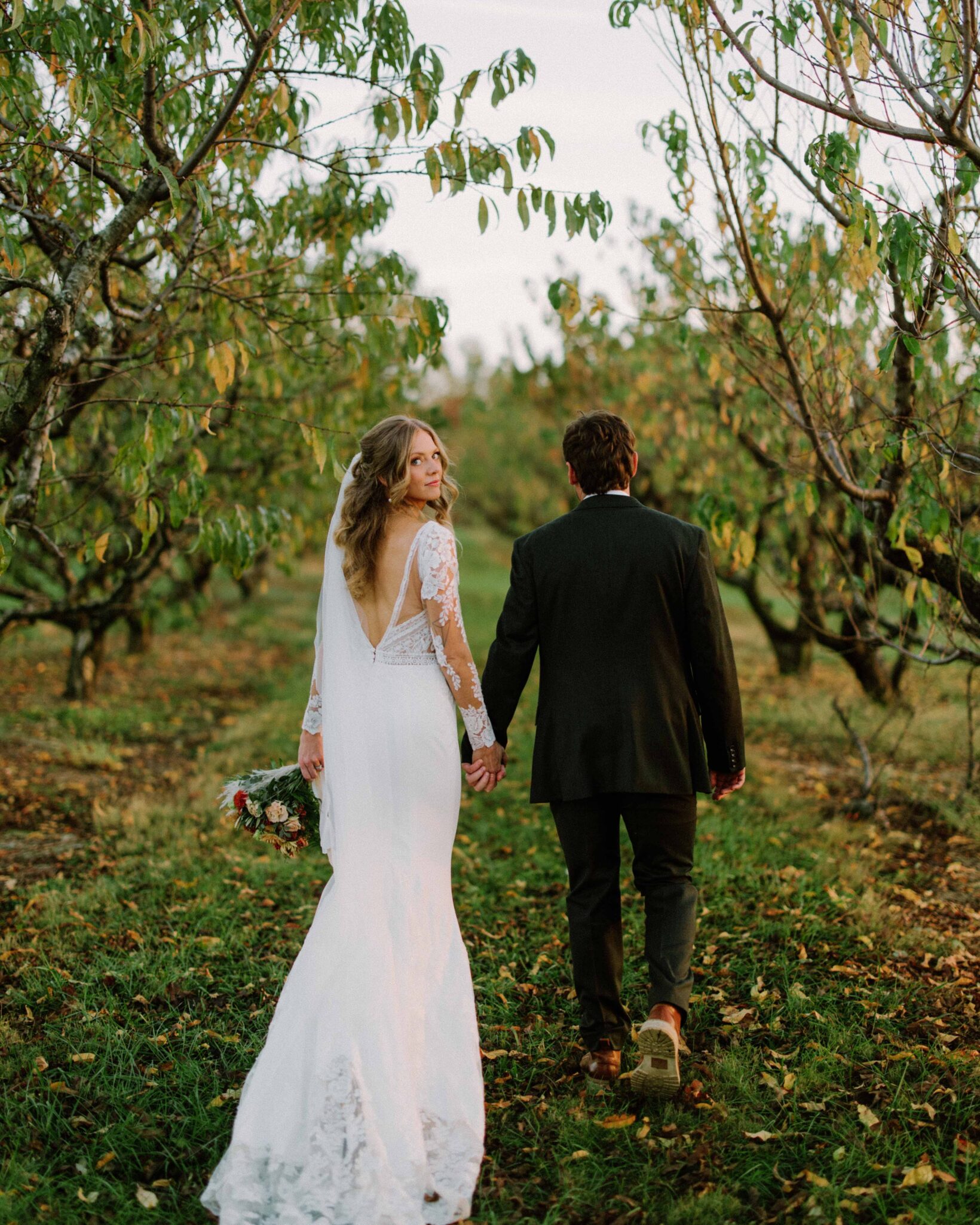 bride and groom walk through and orchard at Chattooga Belle Farm.